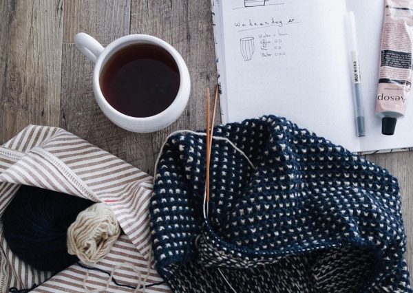 mug of drink, kitting and an open notebook