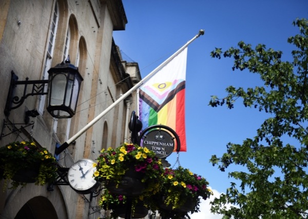 Photograph of the rainbow pride flag hung up outside of chippenham town council with flower hanging baskets