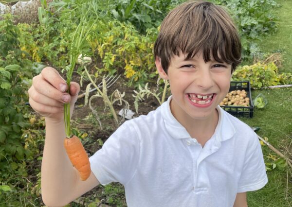 Photograph of a boy in a white t shirt holding up a carrot