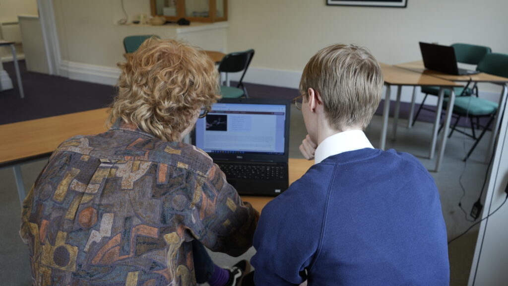 photograph of the back of 2 people looking at a computer screen
