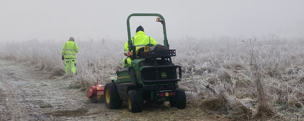 Photograph of 2 people cutting long grass in foggy weather conditions