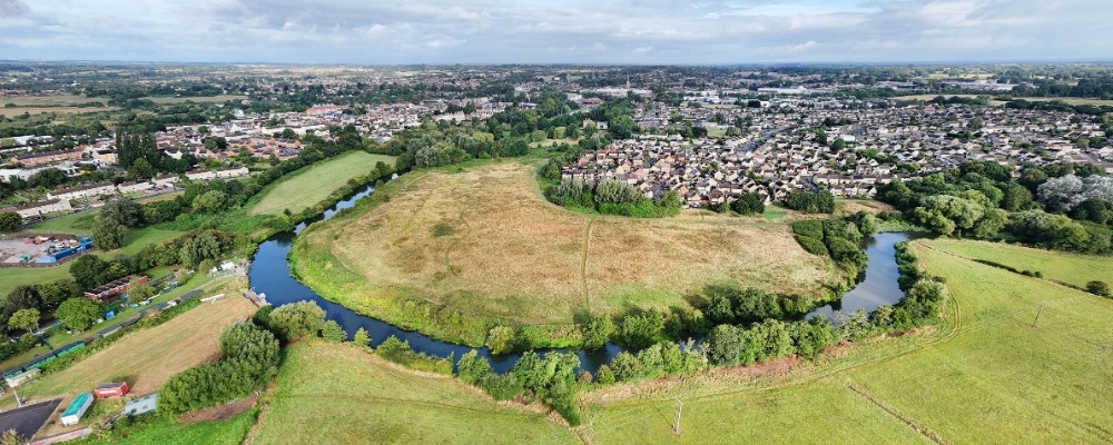 Photograph from above of green fields with a river and houses in the distance