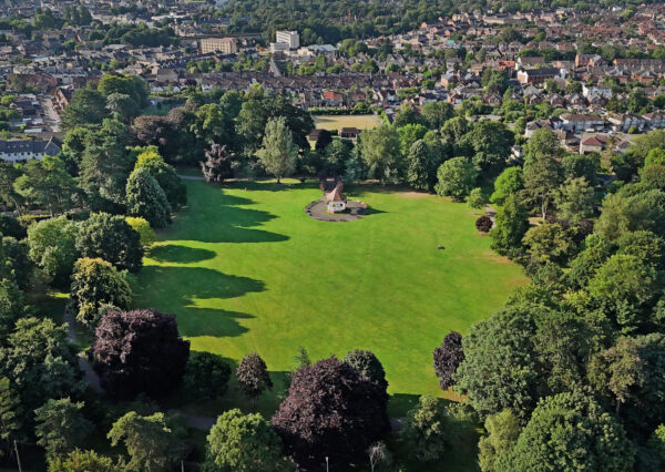 Photograph from above of green grass with lots of trees and a band stand in the middle