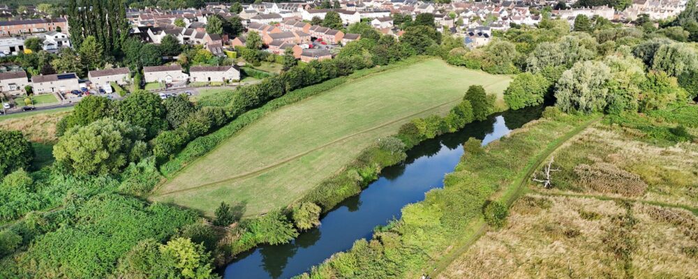 default Photgraph of a small green field with trees and a river