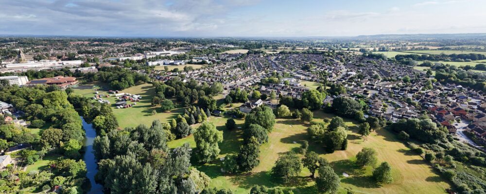default Photograph from above of green fields and trees with a blue sky and lots of houses in the distance