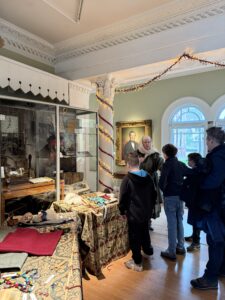 Twelfth Night 2025 A woman in historical clothing talks to a group of children at a museum display with artifacts and textiles.
