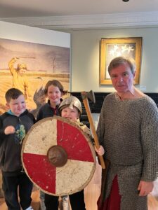 Twelfth Night 2025 Man in Viking costume with three smiling children, one holding a shield and helmet.