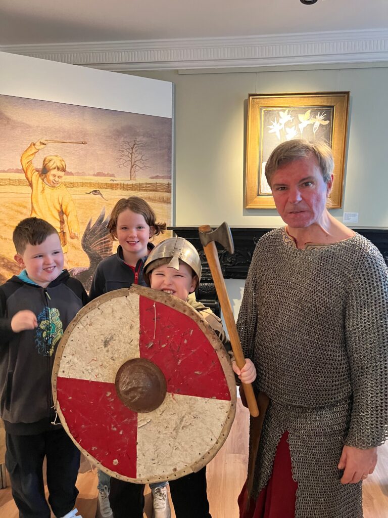 Man in Viking costume with three smiling children, one holding a shield and helmet.
