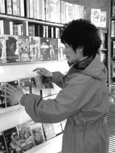 Black and white film photograph from the 2000s showing a woman in a local video shop. Black and white film photograph from the 2000s showing a woman in a local video shop.