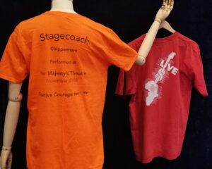 Orange Stagecoach t shirt on a mannequin, with a red t shirt hanging from its hand.
