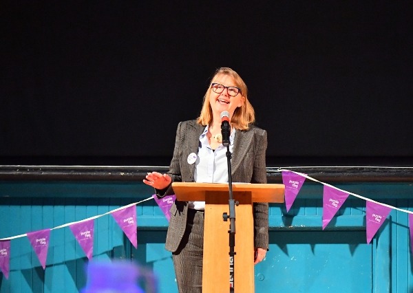 Purple Flag Breakfast A person stands at a lectern speaking to the room, with purple bunting across the front of the stage and a dark backdrop behind them.
