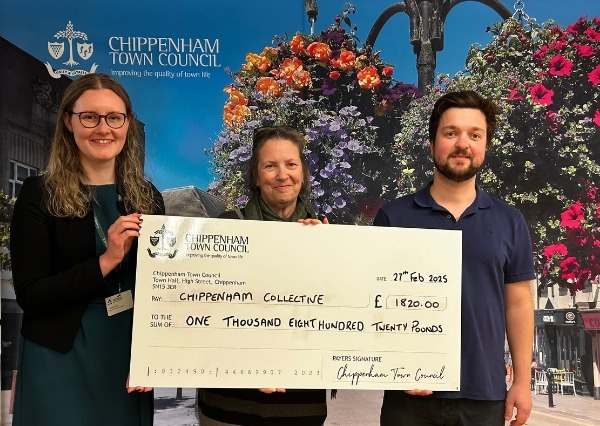 Council Grants Scheme Three people stand smiling in front of a Chippenham Town Council backdrop, holding a large check awarding £1820.00 to Chippenham Collective