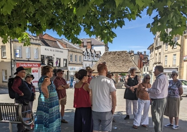 A group of people standing in a market place listening to a guide.