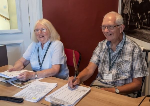 A man and a woman sitting on the front desk at Chippenham Museum. Both are smiling.