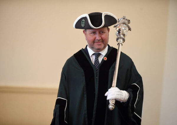A man wearing traditional ceremonial macebearer robes, including a formal tunic and ornate ceremonial attire