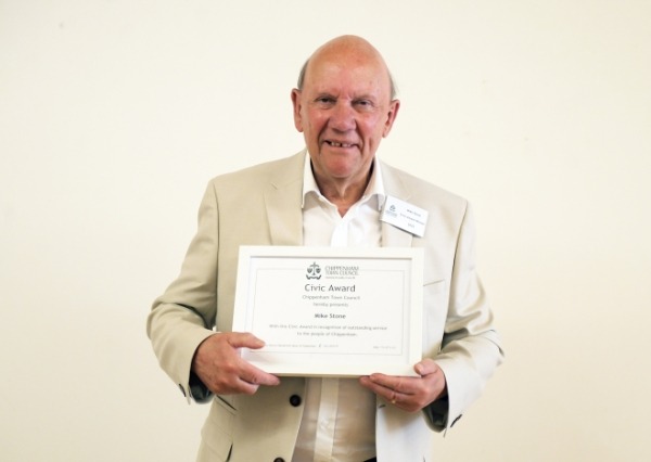 Civic awards A smiling bald man in a light jacket holds a framed civic award certificate toward the camera.