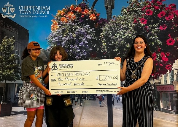 Two people stand smiling in front of a Chippenham Town Council backdrop, holding a large check awarding £1600 Protectors Grant June 2025 Two people stand smiling in front of a Chippenham Town Council backdrop, holding a large check awarding £1600 to Protectors Grant June 2025