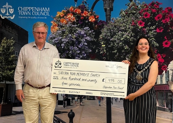 Two people stand smiling in front of a Chippenham Town Council backdrop, holding a large check awarding £995 Sheldon Road Methodist Church Two people stand smiling in front of a Chippenham Town Council backdrop, holding a large check awarding £995 to Sheldon Road Methodist Church