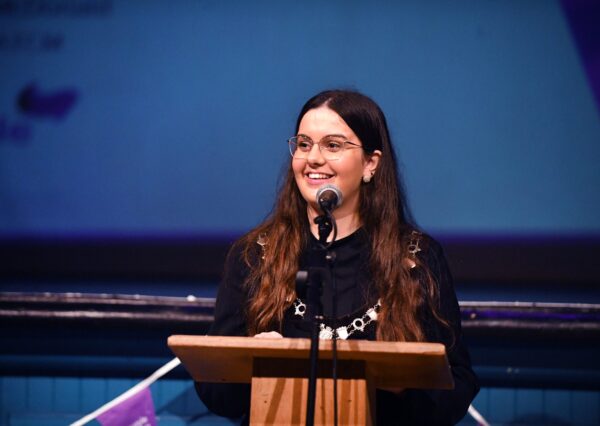 A well dressed woman stands at a podium, speaking into a microphone while addressing an audience. A well dressed woman stands at a podium, speaking into a microphone while addressing an audience.