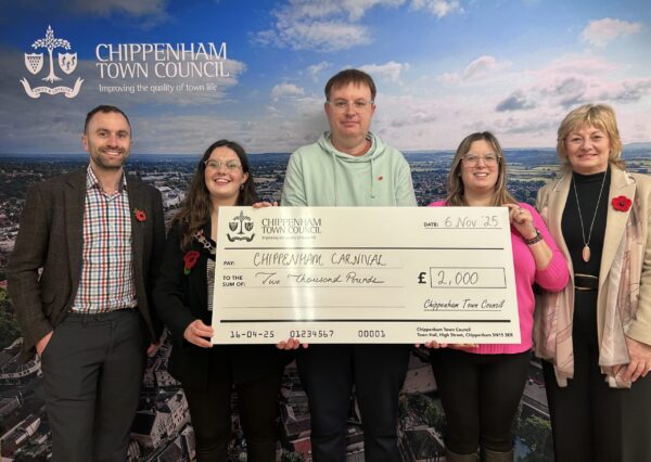 Council Grants Scheme Five people stand smiling in front of a Chippenham Town Council backdrop, holding a large check awarding £2000 to Chippenham Carnival Volunteer Committee