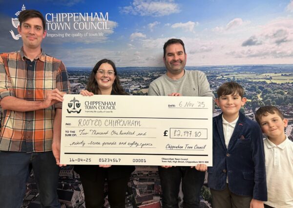 Council Grants Scheme 5 people stand smiling in front of a Chippenham Town Council backdrop, holding a large check awarding £2,197.80 to Rooted Chippenham