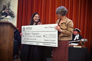 Photograph showing Councillor Kathryn Macdermid and Jane Boulton from Springboard Chippenham holding an oversized check dated 20 May 2026, for £2,139.04. The setting includes a podium with a microphone, a floral arrangement, and a table with a ceremonial mace and nameplate in front of red curtains. Photograph showing Councillor Kathryn Macdermid and Jane Boulton from Springboard Chippenham holding an oversized check dated 20 May 2026, for £2,139.04. The setting includes a podium with a microphone, a floral arrangement, and a table with a ceremonial mace and nameplate in front of red curtains.