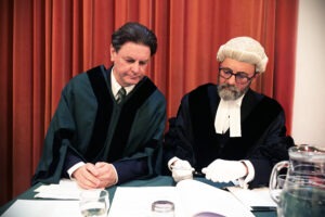 Photograph of Councillor Matthew Bragg, wearing a green Council robe, and Chief Executive Mark Smith wearing official attire, seated at a table signing documents. Behind is a red curtain backdrop. Photograph of Councillor Matthew Bragg, wearing a green Council robe, and Chief Executive Mark Smith wearing official attire, seated at a table signing documents. Behind is a red curtain backdrop.