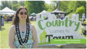 Councillor Kathryn Macdermid, wearing a mayoral chain, stands in front of a 'Country comes to Town' sign at an outdoor event. Councillor Kathryn Macdermid, wearing a mayoral chain, stands in front of a 'Country comes to Town' sign at an outdoor event.