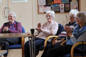 Four older people sitting around a table clapping and smiling to the music. Four older people sitting around a table clapping and smiling to the music.