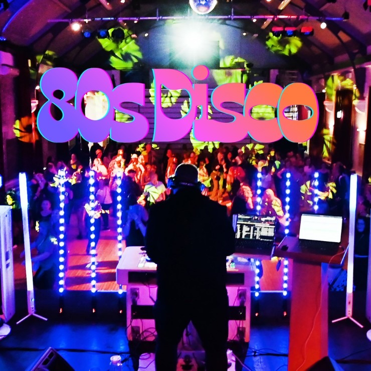 Photograph of a nightclub scene featuring a DJ performing in front of a crowd with vibrant blue and purple lighting. Large, colourful "80s Disco" text overlays the top centre, highlighting the event's theme and retro atmosphere.