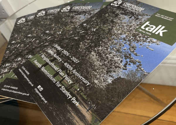 Talk image Photograph of multiple copies of a community newsletter titled "talk Spring 2023" from Chippenham Town Council, featuring a cover photo of a tree-lined path with blooming flowers under a blue sky. The newsletter highlights topics such as the 2026-2027 budget, 400th anniversary of John Mulberry, neighborhood plan policy, and awards nominations for Stanley Park.