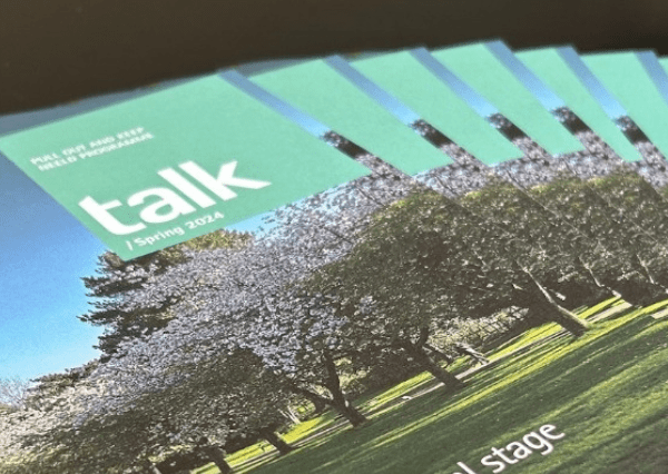 Talk image Photograph of multiple copies of a magazine titled "talk | Spring 2024" featuring a cover image of blossoming trees in a park setting. The magazines are arranged in a fanned-out pattern, highlighting the seasonal theme and outdoor scenery.