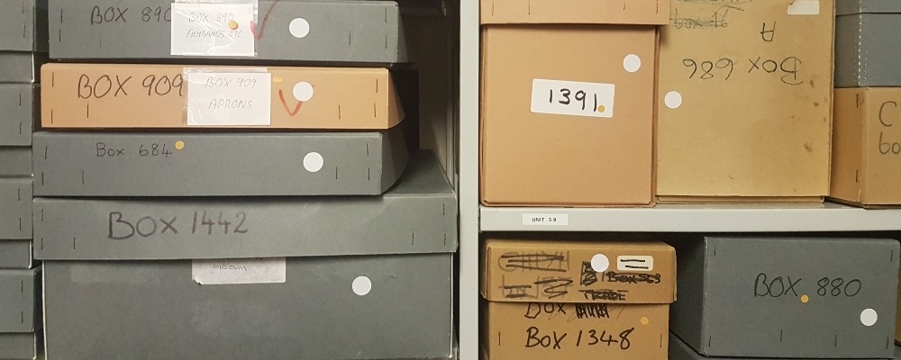 What's in Store exhibition An image of a museum store, with labelled grey and brown boxes of objects on shelves.